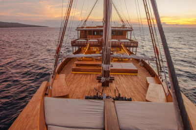 A wooden schooner glides across the calm ocean at sunset, its decks illuminated by warm lights.