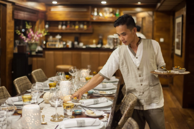 A server carefully places a small appetizer at a beautifully set dining table in a richly decorated room.