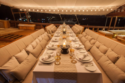 A beautifully set dinner table awaits guests on a luxurious yacht deck under a canopy of twinkling lights.