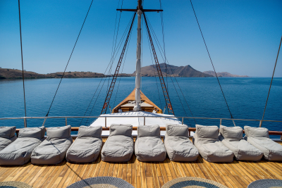 Relax on comfortable lounge chairs on the deck of a traditional wooden sailboat while cruising through calm blue waters.