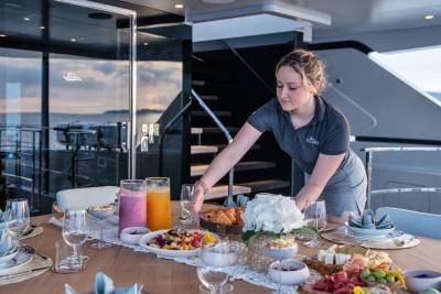 A server arranges a delightful breakfast spread of fruits, pastries, and cheeses on a yacht deck.