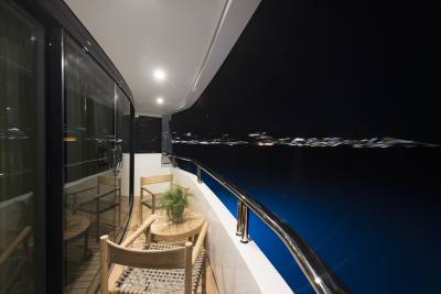 A tranquil night unfolds on the yacht's deck, with distant city lights shimmering across the dark, calm water.