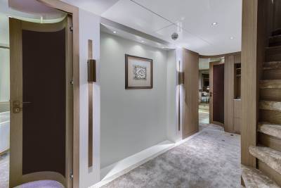 A luxurious yacht hallway features elegant wood accents, soft carpeting, and subtle lighting leading to a plush staircase.