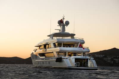 A luxurious yacht named Liquid Sky sails on calm waters under a warm, dusky sky near a coastal town.
