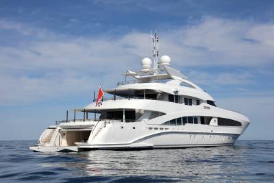 A luxurious white yacht named COMO glides serenely across the calm blue ocean under a bright, cloudy sky.