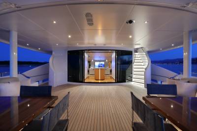 Evening lights illuminate the luxurious deck of a yacht, featuring elegant seating, dining areas, and a striking spiral staircase.
