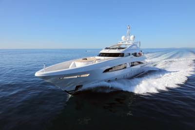A sleek white superyacht glides through the deep blue ocean, leaving a foamy white wake under a clear sky.