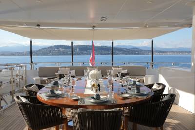 An elegant outdoor dining setting on a yacht overlooks a picturesque coastal town.
