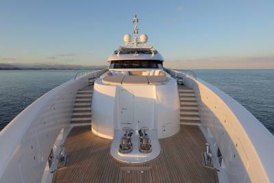 The sun casts a warm glow on the pristine deck of a luxurious yacht as it glides across the calm, blue sea.