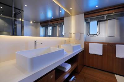 This luxurious yacht bathroom features sleek white vessel sinks, a large mirror, and a porthole window with a stunning ocean view.