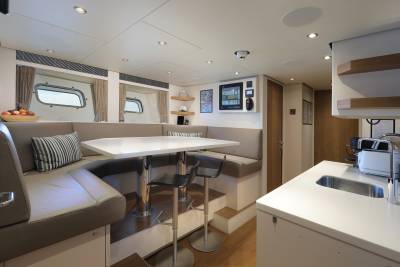 A modern yacht interior features a comfortable dining area with a U-shaped sofa and a sleek white table adjacent to a compact kitchen.