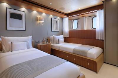 Two twin beds with crisp white linens and grey throws are neatly made in this luxurious yacht cabin.