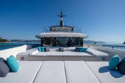 Luxurious white cushions and vibrant teal pillows adorn the deck of a yacht, offering a serene spot to enjoy the stunning coastal scenery.