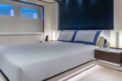 Luxurious yacht cabin features a plush bed, modern bedside lamps, and illuminated porthole windows.