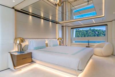 Luxurious yacht bedroom offers stunning views of lush green hills through a panoramic window.