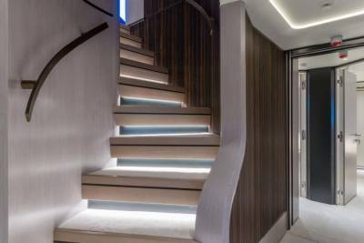 A modern staircase with illuminated treads curves elegantly upwards, leading to a hallway with sleek doors.