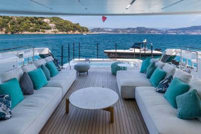 Luxurious white sofas and turquoise cushions offer a serene seating area on a yacht deck with a stunning coastal view.