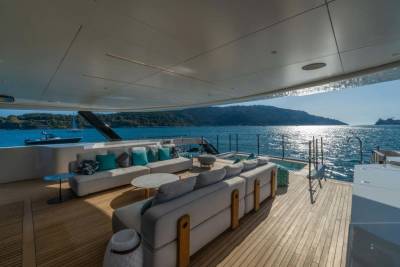 Relax on the plush outdoor seating of this luxurious yacht while enjoying the sparkling sea and distant, tree-covered hills.