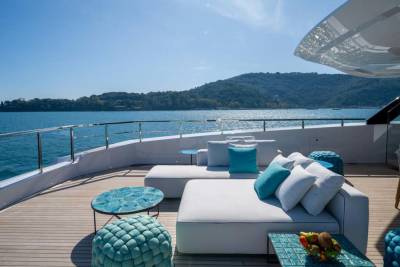 Relax on the plush white loungers of this luxurious yacht deck, overlooking a serene blue bay and lush green hills.