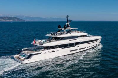 A sleek white superyacht glides through the deep blue ocean under a clear sky.