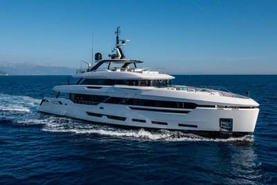 A sleek white superyacht glides through deep blue waters under a clear sky.
