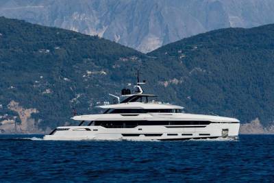 A sleek white yacht glides through the deep blue sea with a lush, mountainous coastline in the background.