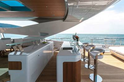Luxurious yacht deck features a sleek bar with stools, dining area, and sun loungers overlooking the serene ocean.
