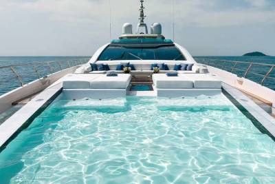 A luxurious yacht features a stunning infinity pool with crystal-clear water, set against the backdrop of the open sea and a hazy coastline.