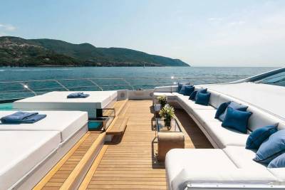 Luxurious white sunbeds and plush blue cushions adorn the deck of this yacht, offering a serene spot to relax by the sparkling sea.