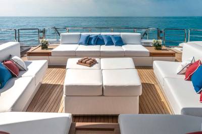 Luxurious white sofas with red, white, and blue pillows adorn the deck of a yacht overlooking the tranquil blue sea.
