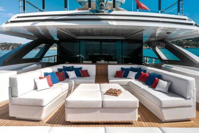 Luxurious white sofas with red and blue cushions adorn the deck of this elegant yacht, overlooking a serene blue sea.