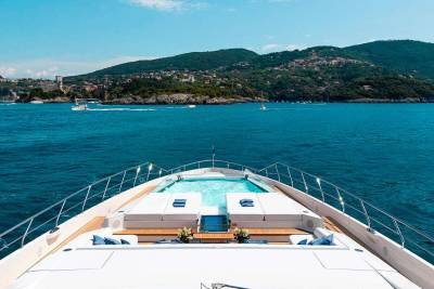 A luxurious yacht with a pristine pool cruises through the vibrant blue waters off a picturesque, verdant coastline.