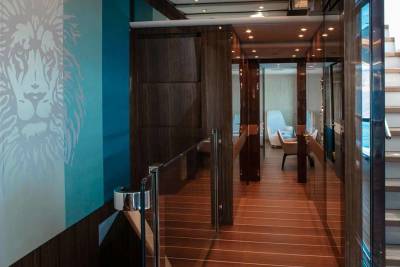 A majestic lion mural adorns the wall of this luxurious yacht's hallway, leading to elegant seating areas and a sun-drenched staircase.