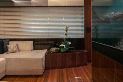 Luxurious yacht interior features a plush sectional sofa, elegant blinds, and a stunning mountain and lake vista displayed on a large screen.