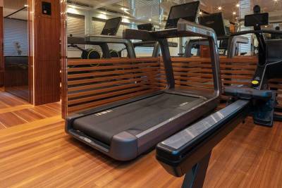 A modern gym on a yacht features treadmills and rowing machines with sleek wood accents and mirrored walls.