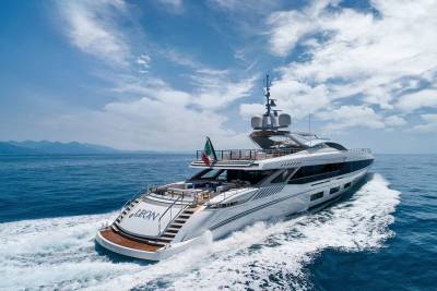 A sleek white yacht named Leon cruises through the azure waters under a brilliant blue sky dotted with fluffy clouds.
