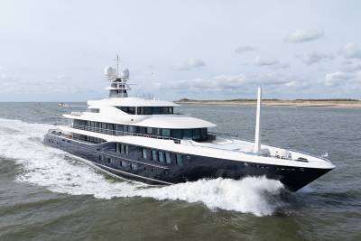 A sleek, dark-hulled superyacht cuts through choppy waters under a cloudy sky.