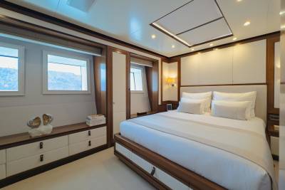 Luxurious yacht cabin features a spacious bed, elegant wood accents, and stunning ocean views from the windows.