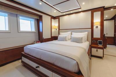 Luxurious yacht bedroom features a king-sized bed, elegant wood accents, and calming natural light from the porthole windows.