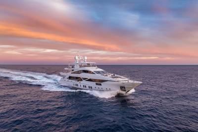 A luxurious white yacht glides through the deep blue ocean under a vibrant sunset sky.