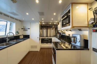 A modern yacht galley features sleek white cabinetry, stainless steel appliances, and a large window overlooking a scenic view.