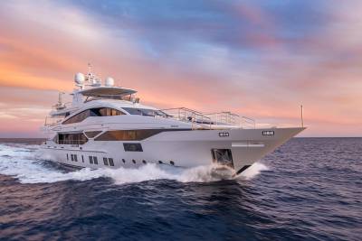 A luxurious white yacht glides through the ocean waves under a vibrant sunset sky.