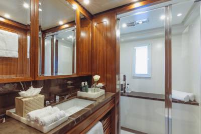 A luxurious yacht bathroom features a marble vanity, a glass-enclosed shower, and rich wood cabinetry.