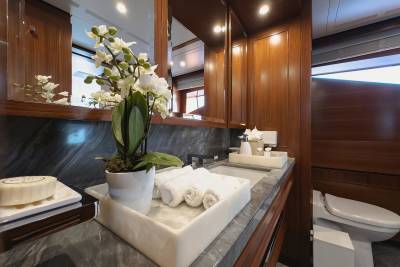 A luxurious yacht bathroom features a marble countertop, a white orchid, rolled towels, and a sleek toilet.