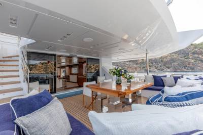 Luxurious outdoor seating and dining areas on a yacht offer a stunning view of a rocky coastline.