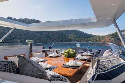 A beautifully set dining table awaits guests on a yacht's deck, overlooking a picturesque bay.