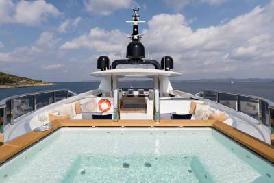A luxurious yacht's sundeck features a sparkling jacuzzi and plush seating overlooking a serene coastal landscape.