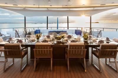 A beautifully set dining table awaits guests on the deck of a luxury yacht at sunset.