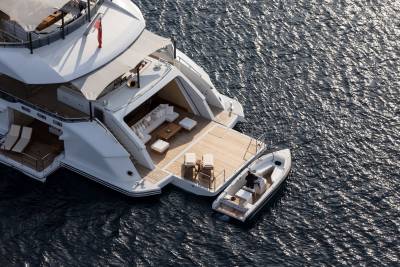 A luxurious yacht with an open deck and a tender boat docked alongside floats on the shimmering blue sea.