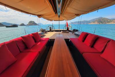 Luxurious red cushions invite relaxation on the deck of this elegant yacht, cruising through turquoise waters amidst scenic islands.